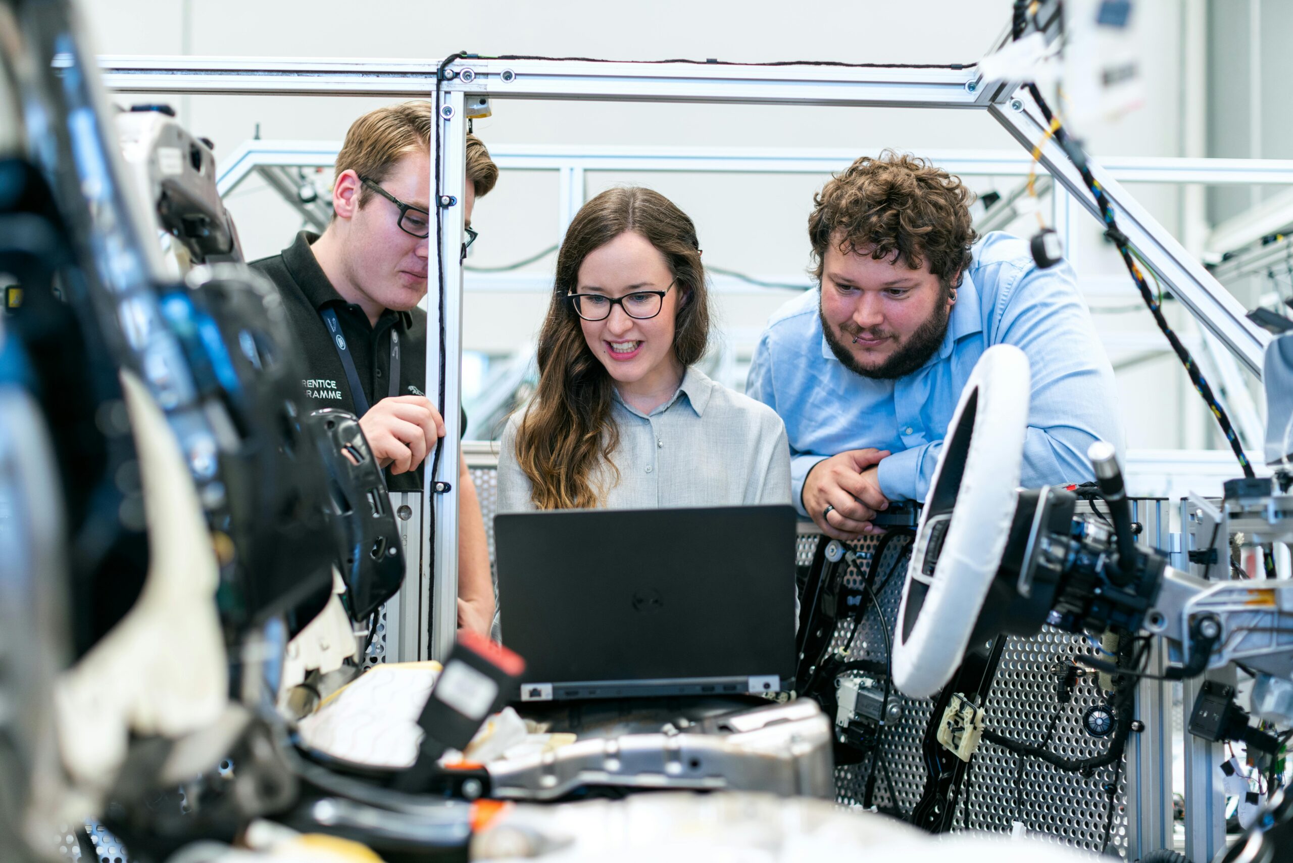 Three employees looking at a laptop together in an industrial workspace.