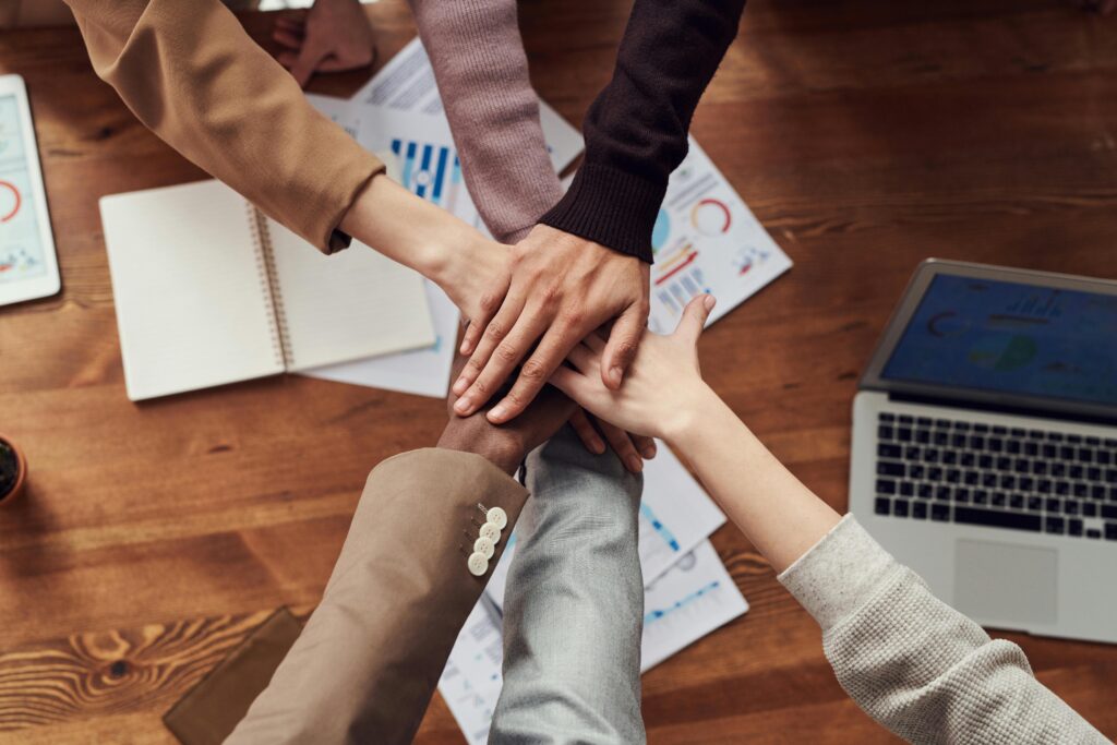 A close up of a team with their hands stacked together over a desk at work.