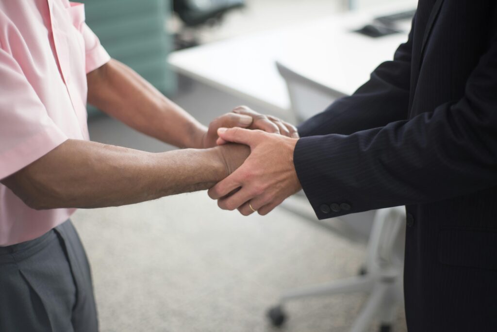 A close up of two people standing in an office, one is holding the other persons hands in front of them.