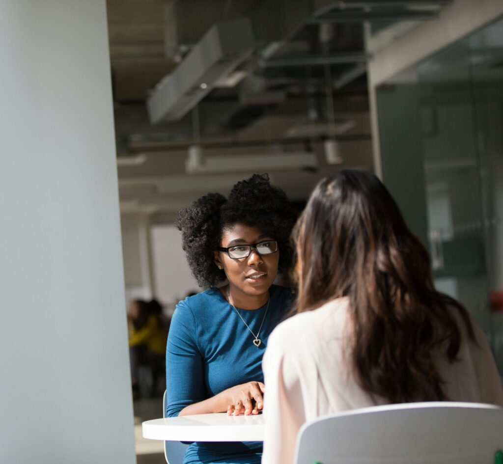 Two female colleagues sitting at a table together to have a conversation.